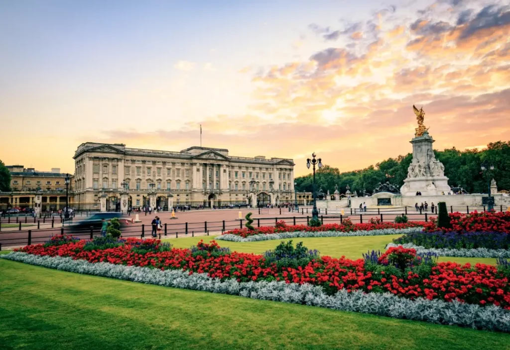 People gather around a large fountain with a golden statue in to, surrounded by a colorful flower garden